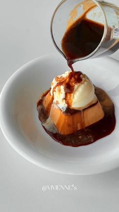 a white plate topped with ice cream and caramel sauce next to a cup filled with syrup