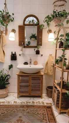 a white sink sitting under a mirror next to a wooden shelf filled with potted plants