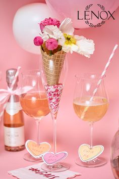 three wine glasses with flowers in them on a pink surface next to balloons and confetti