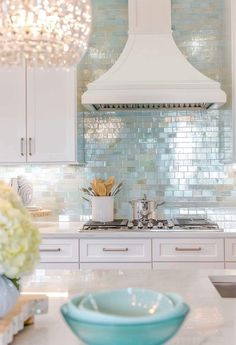 a white kitchen with blue glass backsplash and chandelier over the stove