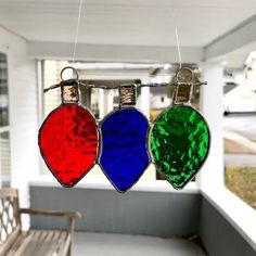 three stained glass ornaments hanging from a line on a porch with a bench in the foreground