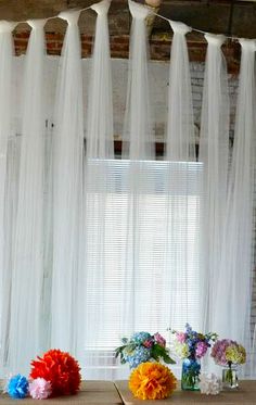 some flowers are sitting on a table in front of a window with sheer drapes