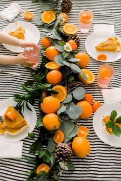 the table is set with oranges and pine cones on it, along with plates