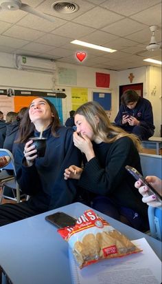 two women sitting at a table laughing and holding their cell phones in front of them