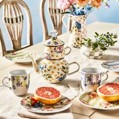 a table topped with plates and cups filled with fruit next to a vase full of flowers