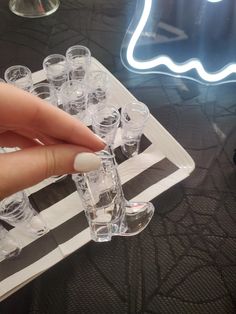 a hand is pointing at some wine glasses on a glass tray with lights in the background