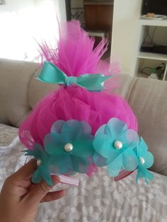 a hand holding two pink and blue flowers on top of a bed next to a couch