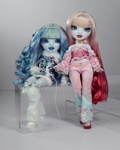 two dolls sitting next to each other on a chair