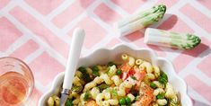 a bowl of pasta with shrimp and asparagus next to two wine glasses on a pink tablecloth