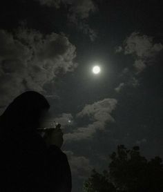 a person is looking up at the moon in the night sky with clouds and trees