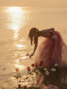 a woman in a red and white dress is standing in the water with her hands on flowers