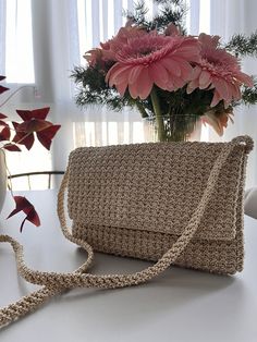 a crocheted purse sitting on top of a table next to a vase with flowers