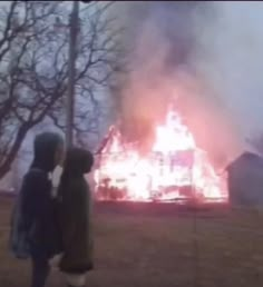 two people standing in front of a house on fire