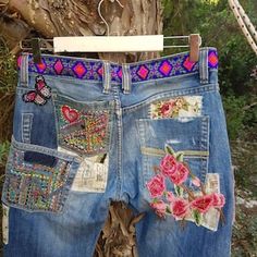 a pair of blue jeans with embroidered patches and flowers on them hanging from a tree