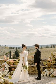 a bride and groom standing next to each other in front of a stone wall with flowers