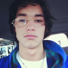 a young man wearing glasses and a blue jacket in the back seat of a car