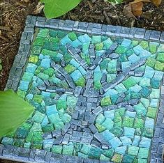 a tree made out of small rocks and green leaves on the ground next to some plants