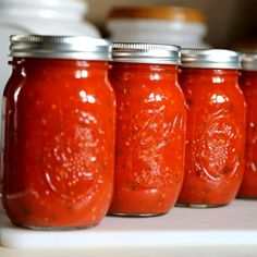 four jars filled with red sauce sitting on top of a counter