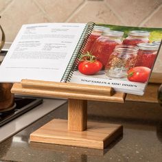 a recipe book on a wooden stand with tomatoes and canning jars in the back ground