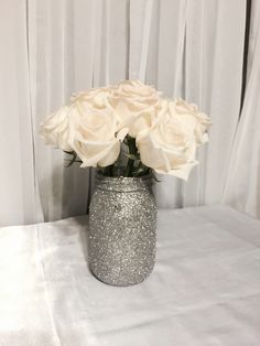 white roses in a silver glitter vase on a table with curtain behind it and curtains