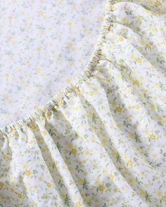 a white and yellow floral print dress with ruffles on the bottom, sitting on top of a bed