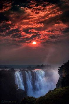 the sun is setting over a large waterfall with water cascading down it's sides