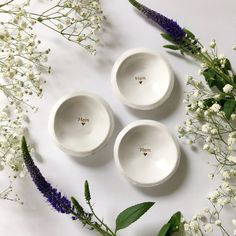 three white bowls sitting on top of a table next to flowers