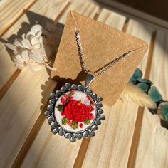 a necklace with a red rose on it sitting on a wooden table next to feathers