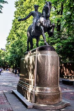 a statue of a man riding a horse on top of a stone pedestal in the middle of a park