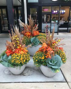 three planters with flowers and plants in them on the sidewalk