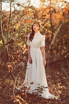 a woman standing in the woods wearing a white dress