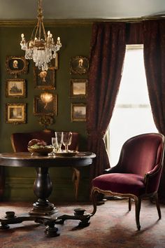 an elegant dining room with green walls and chandelier hanging from the ceiling, along with red velvet upholstered chairs