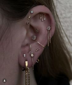 a woman wearing ear piercings with gold chains and beads on her ears, behind the ear