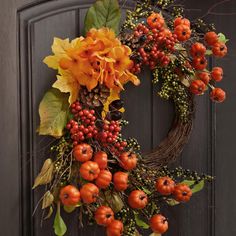 a wreath with orange flowers and berries hanging on the front door to give it an autumn feel