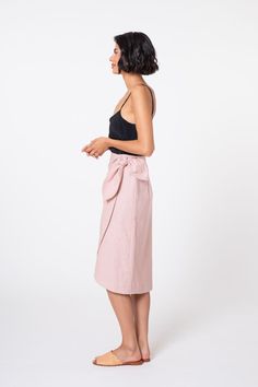 a woman standing in front of a white background wearing a pink skirt and black tank top