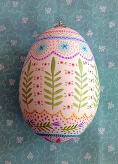 an egg painted with flowers and leaves is hanging on a blue wallpapered background