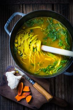 a pot filled with noodles and carrots on top of a wooden table next to a knife