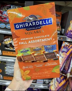 someone holding up a box of ghirardell chocolates in a store aisle