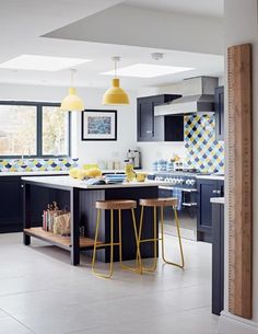 an open kitchen with yellow pendant lights and black cabinets, along with two stools in front of the island