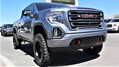 the front end of a silver gmc truck parked in a parking lot next to other cars