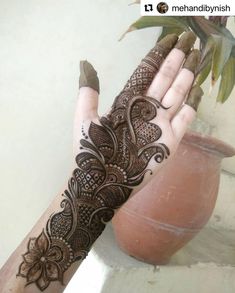 a woman's hand with henna tattoos on it and a potted plant in the background