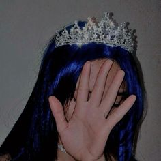 a woman with blue hair wearing a tiara covering her face and holding her hand up to her face