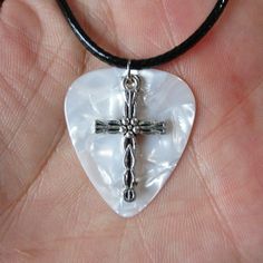 a white heart shaped pendant with a cross in it's center on a black cord