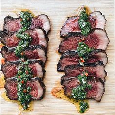 two pieces of meat on a cutting board covered in greens and spices, with one piece being sliced into smaller portions