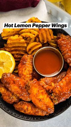 chicken wings, french fries and dipping sauce on a black plate with lemon wedges