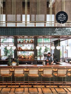 a bar with lots of chairs around it and a man behind the bar making drinks