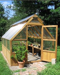 a small wooden greenhouse sitting in the middle of a green field with potted plants