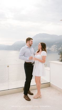 a man and woman standing next to each other on top of a building near the water