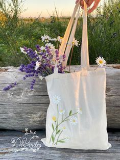 a hand holding a white bag with flowers in it on a wooden table next to a fence