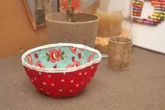 a red and white polka dot bowl sitting on top of a floor next to a potted plant